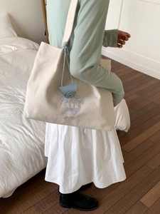 Off-white canvas tote bag with blue embroidery and shoulder strap on female model