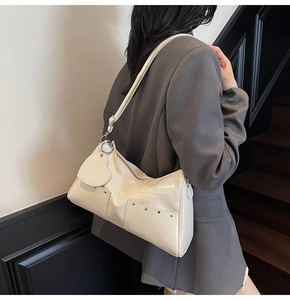 Detail view of cream shoulder bag with heart pendant and silver rivets on the bottom