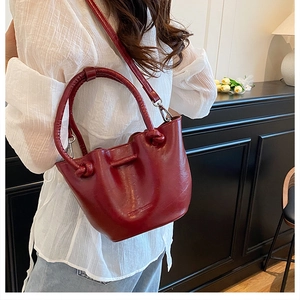 Detailed close-up of a burgundy bucket bag with a round handle and shoulder strap