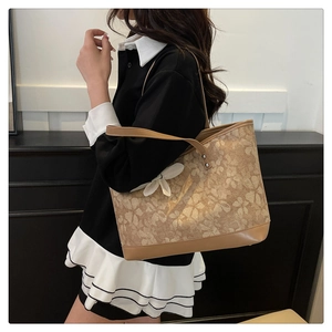 Detail of a large beige floral tote bag with embroidery and a decorative white bow charm