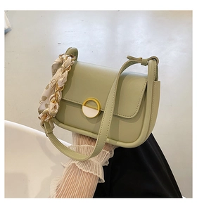 Détail d'un sac selle vert clair avec foulard en soie et boucle ronde dorée