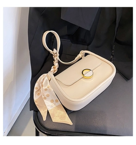 Détail d'un sac selle blanc cassé avec boucle dorée et écharpe décorative en soie