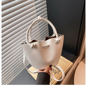 Detail of white lychee leather bucket bag featuring a unique knotted handle and strap