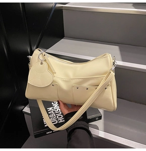 Close-up of cream yellow shoulder bag with silver studs and a heart pendant on a book