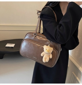 Close-up of retro brown Boston bag featuring a plush bear pendant and leather texture