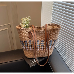 Détail du sac cabas en paille tressée avec poignées en cuir et motifs floraux bleus