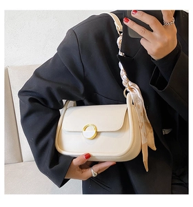 Gros plan d'un sac selle crème avec boucle dorée et foulard en soie sur la bandoulière