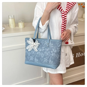 Detail of light blue embroidered tote bag with a white fabric flower charm and FUOR tag