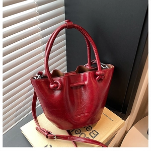 Close-up of deep red bucket bag featuring glossy wrinkled leather texture and handle