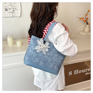 Detail of light blue embroidered tote bag with 3D white floral charm and leather base