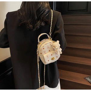 Mini-Rucksack in Beige mit Bärenmuster und Goldkette über einem schwarzen Blazer