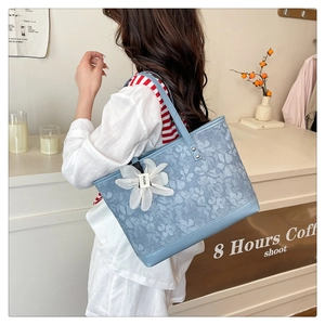 Detail of blue floral tote bag with embroidery, leather trim, and white flower charm