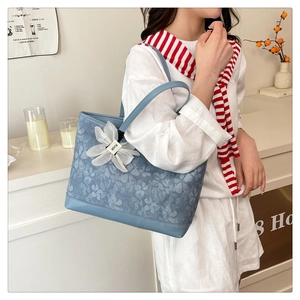 Detail of blue floral embroidered tote bag with white flower charm and metal hardware