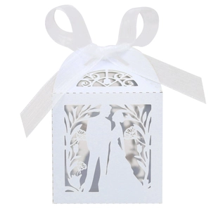Close-up of laser-cut white wedding favor box with silk ribbon and bride groom silhouettes