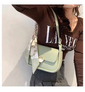 Détail du sac de selle en cuir vert menthe avec boucle dorée et foulard en soie à cerises