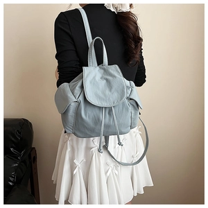 Detail of light blue nylon backpack with drawstring closure and side pockets on model