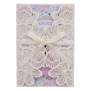 Close-up of laser-cut wedding invitation with cream hollow shell and satin ribbon bow