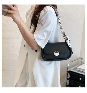 Détail d'un sac selle en cuir noir avec boucle dorée et foulard floral sur l'anse