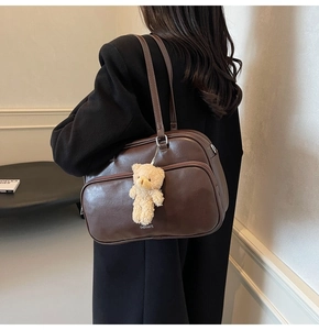 Detail of a large dark brown faux leather pillow bag with cute plush bear charm accessory