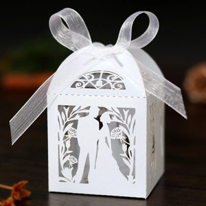 Detail of white laser-cut wedding favor box with bride and groom silhouette and ribbon