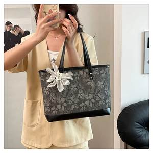 Detail of grey floral embroidery tote bag with black leather base and flower pendant