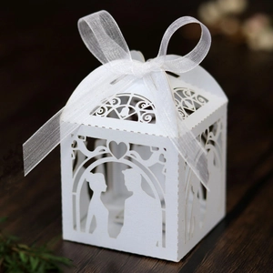 Macro shot of white laser-cut wedding favor box with ribbon on wooden background