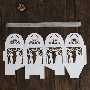 Flat lay of laser-cut wedding candy box with heart pattern and silver ribbon on wood