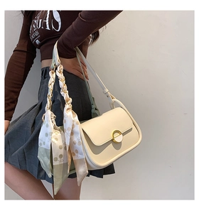 Gros plan sur un sac selle crème avec fermoir doré et foulard en soie porté par un mannequin