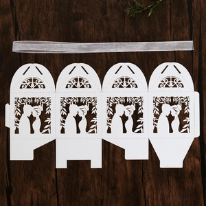 Flat lay of laser-cut wedding favor box with white ribbon on dark wooden background
