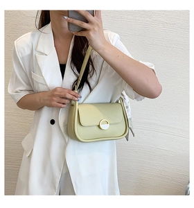Détail du sac besace vert clair en cuir avec boucle dorée sur un blazer blanc