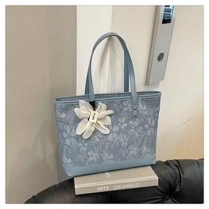 Detail of blue floral canvas tote bag featuring leather handles and a 3D flower charm accessory