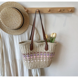 Détail d'un sac cabas en paille tressée avec motifs ondulés et anses en cuir brun