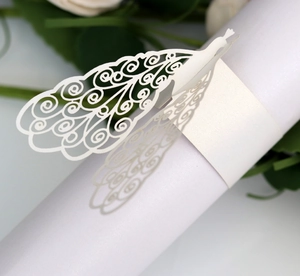 Detail of laser-cut white paper peacock napkin ring with intricate spiral patterns for weddings