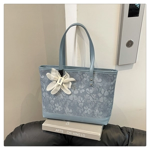 Detail of light blue floral jacquard tote bag with mesh flower charm on a book