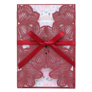 Detail of burgundy laser-cut wedding invitation with floral insert and satin bow ribbon