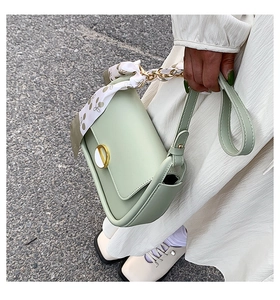 Détail du sac selle vert menthe avec boucle dorée et foulard en soie sur la poignée