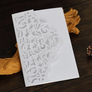 Detail showing white laser-cut floral wedding invitation card on wooden background