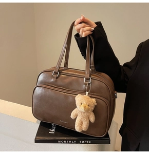 Detail of vintage brown leather handbag with exterior pocket and plush bear charm accessory