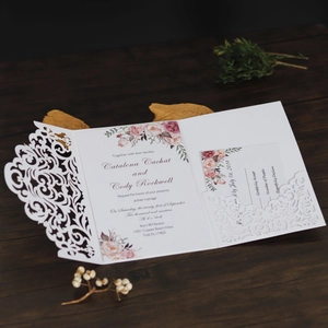 Macro shot of laser-cut floral wedding invitation set on dark wood table surface