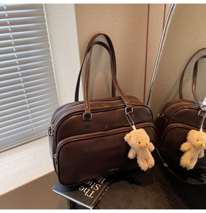 Detail of dark brown leather boston bag with double zipper and plush bear charm