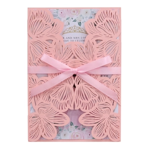 Detail of pink laser-cut wedding invitation with elegant floral patterns and silk bow