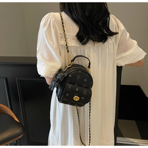 Detailansicht eines schwarzen Mini-Rucksacks mit Logomuster, Kette und Bärenanhänger
