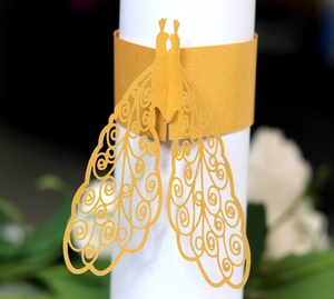 Macro view of a laser-cut gold peacock paper napkin ring for elegant wedding table decor
