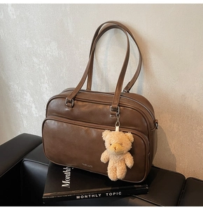 Detail of brown leather Boston bag with plush bear charm on a dark leather background