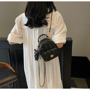 Rückansicht eines schwarzen Mini-Rucksacks mit Bärenmuster und Kette auf weißem Kleid