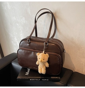 Detail of deep brown Boston bag with metal zippers and a plush bear charm on a sofa
