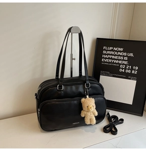 Close-up of black leather Boston bag with plush bear charm on a marble surface