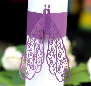 Elegant purple laser-cut paper napkin rings with detailed peacock wings for wedding decor