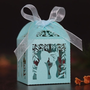 Detail of laser-cut wedding favor box in light blue with ribbon bow and couple silhouette