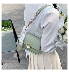 Détail du sac selle vert clair avec bandoulière en chaîne dorée et foulard en soie